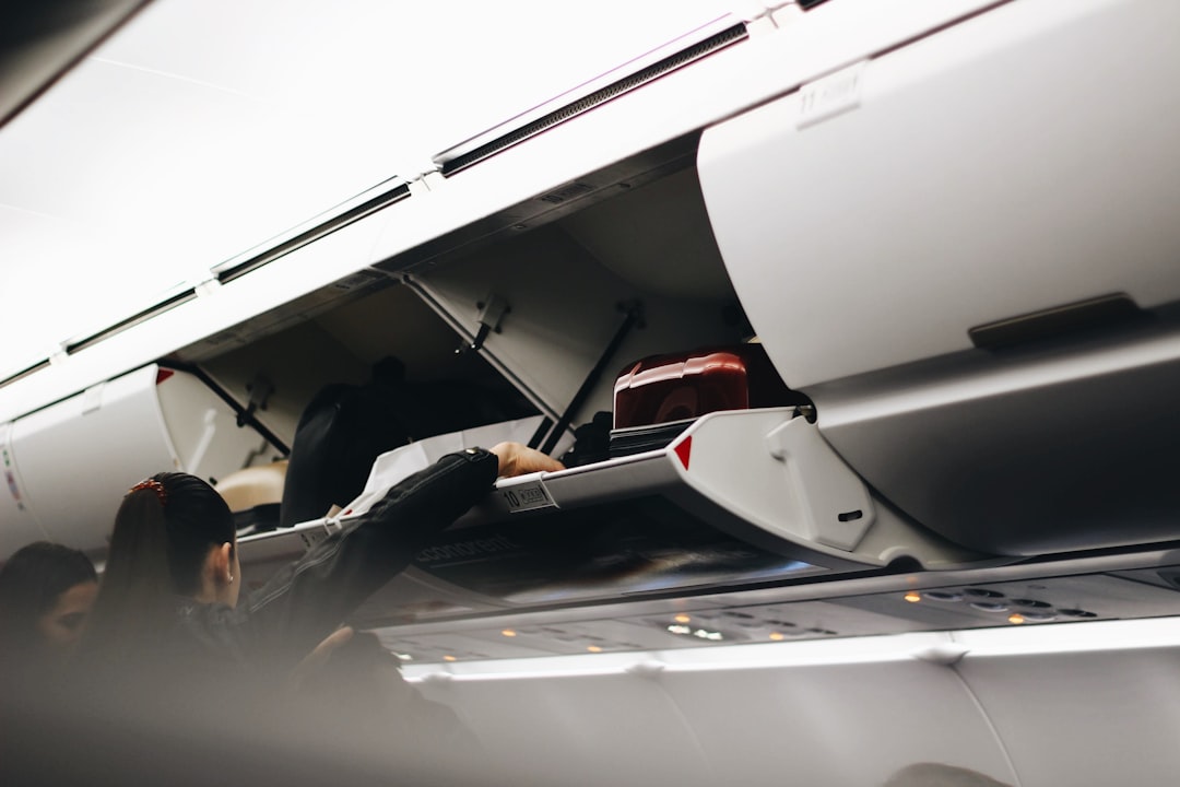 Person placing a carry-on bag into an airplane overhead bin, demonstrating carry-on only travel to avoid baggage fees