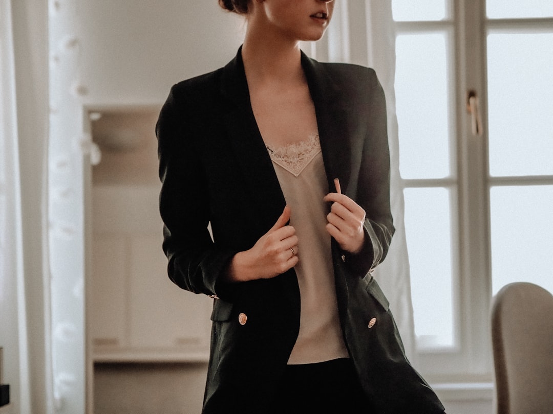 Woman wearing a black blazer layered over a light camisole, showing how layering covers bra straps at the shoulder area