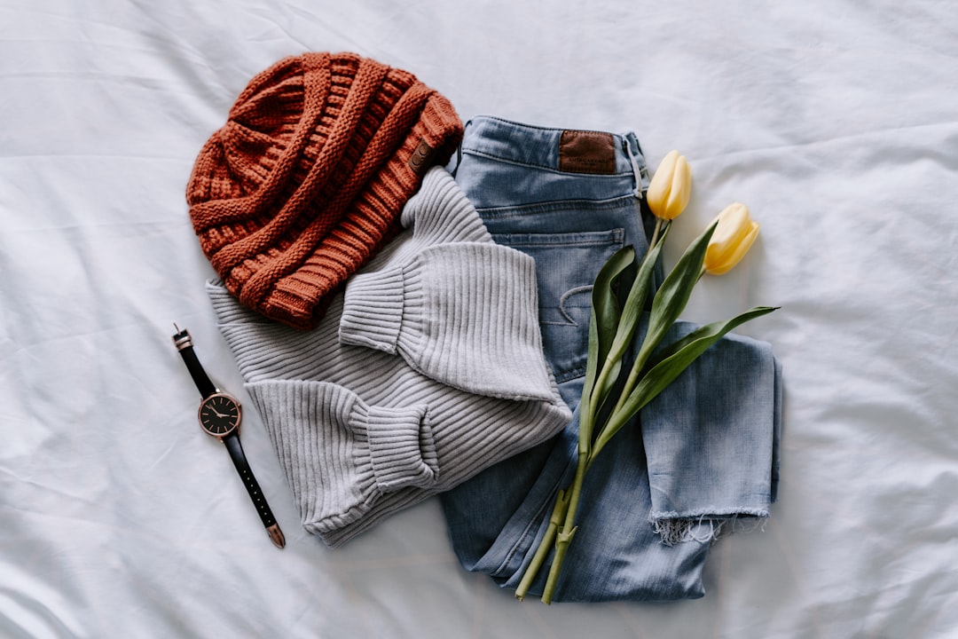 Flat lay of a capsule wardrobe showing a coordinated outfit with grey sweater, jeans, knit hat, and watch on a white bed