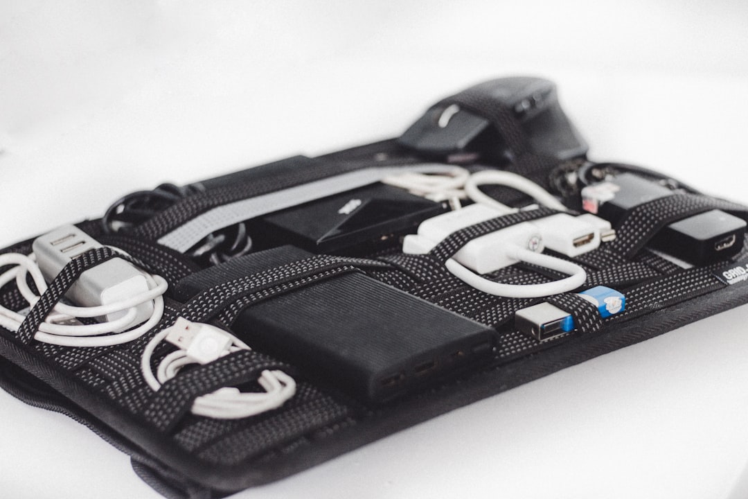 Black electronics organizer pouch with charging cables, power bank, USB drives, and mouse secured by elastic straps