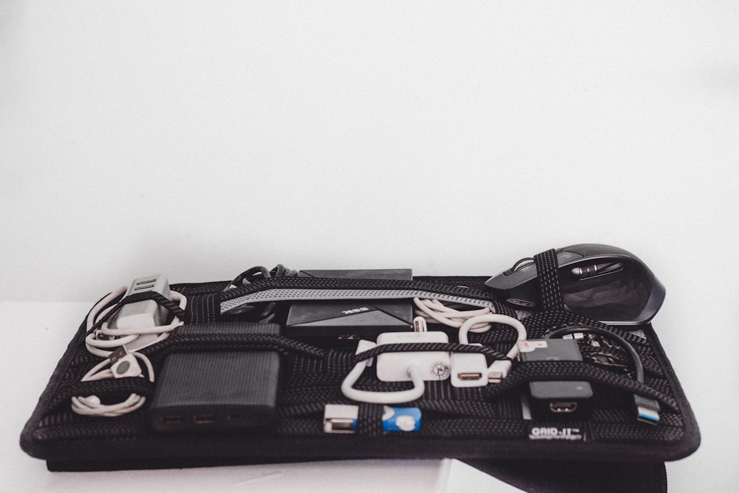 Electronics organizer showing cables, power bank, mouse, and adapters organized on a black grid board with elastic straps