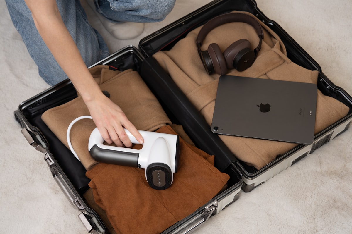 Close-up of a portable garment steamer being placed into a suitcase filled with neatly folded clothes and travel essentials
