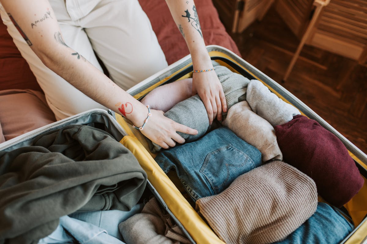 Woman organizing and rolling clothes to pack into an open carry-on suitcase