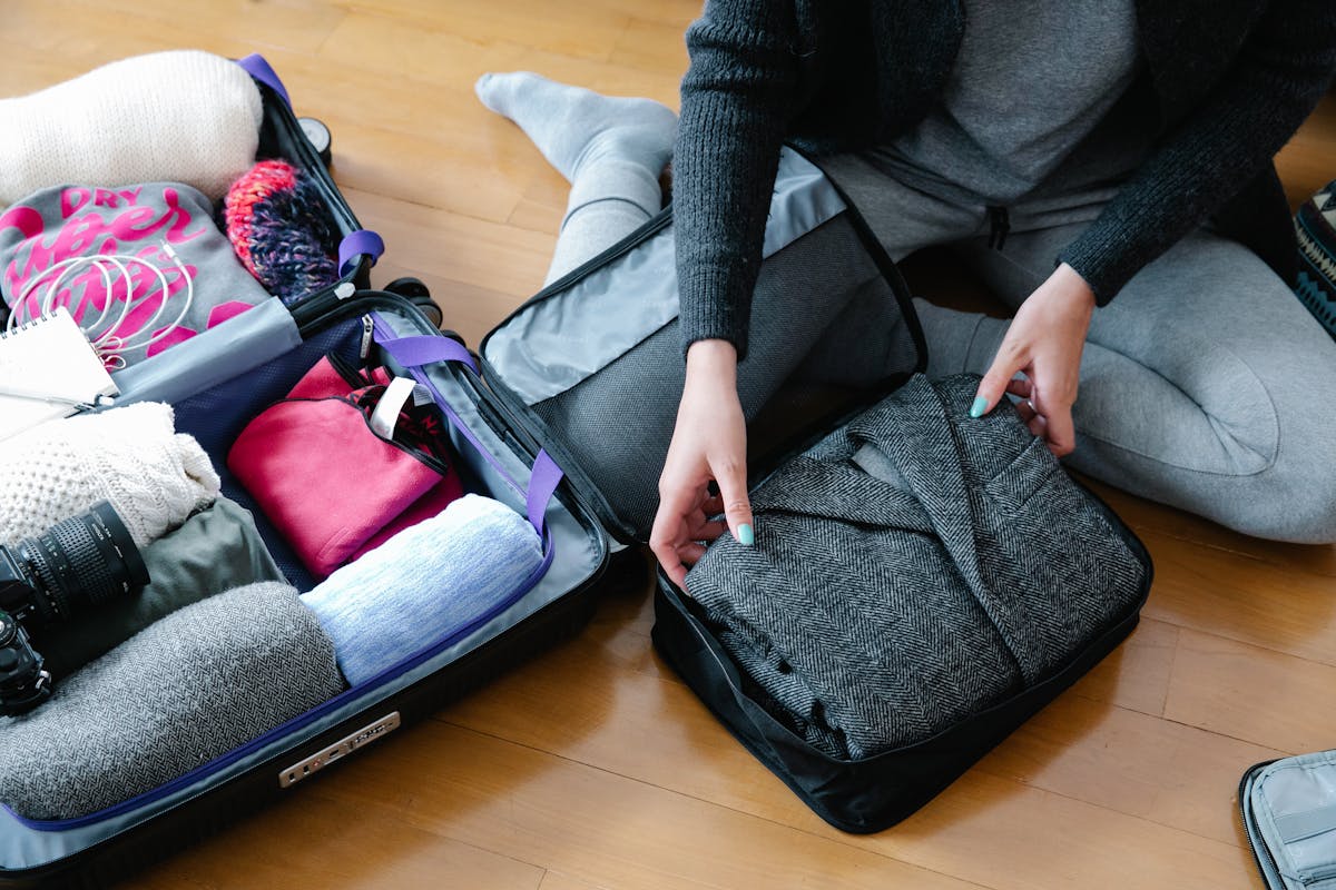 Person placing folded clothes into mesh packing cubes inside an open suitcase