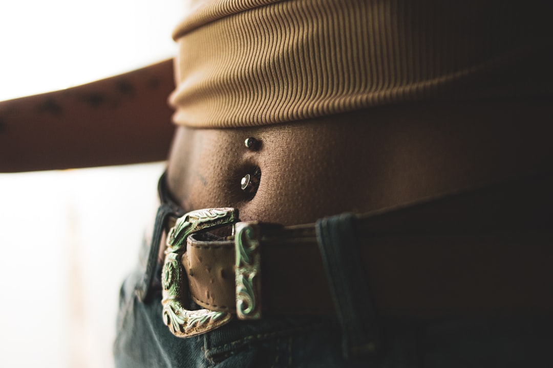 Close-up of a belly button piercing visible between a crop top and low-rise jeans, demonstrating how clothing choices show off body piercings