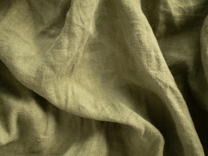 Close-up of wrinkled olive green linen fabric showing deep creases that form when natural fibers are compressed