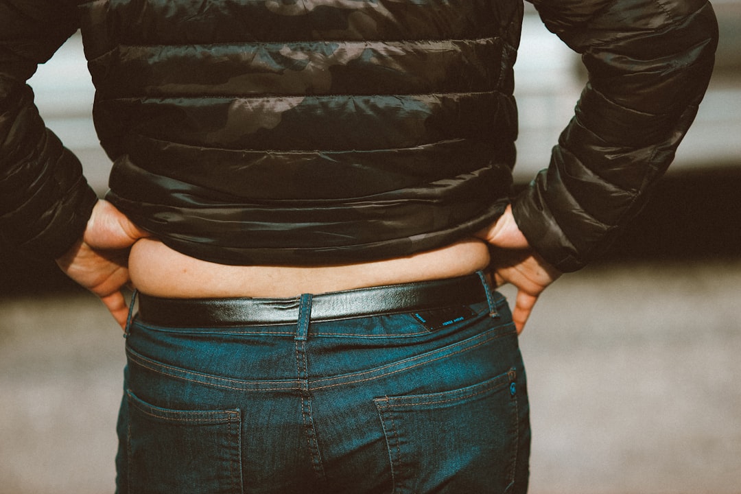 Person seen from behind adjusting their jeans waistband where the pants sit below the natural waist showing the most common cause of pants falling down