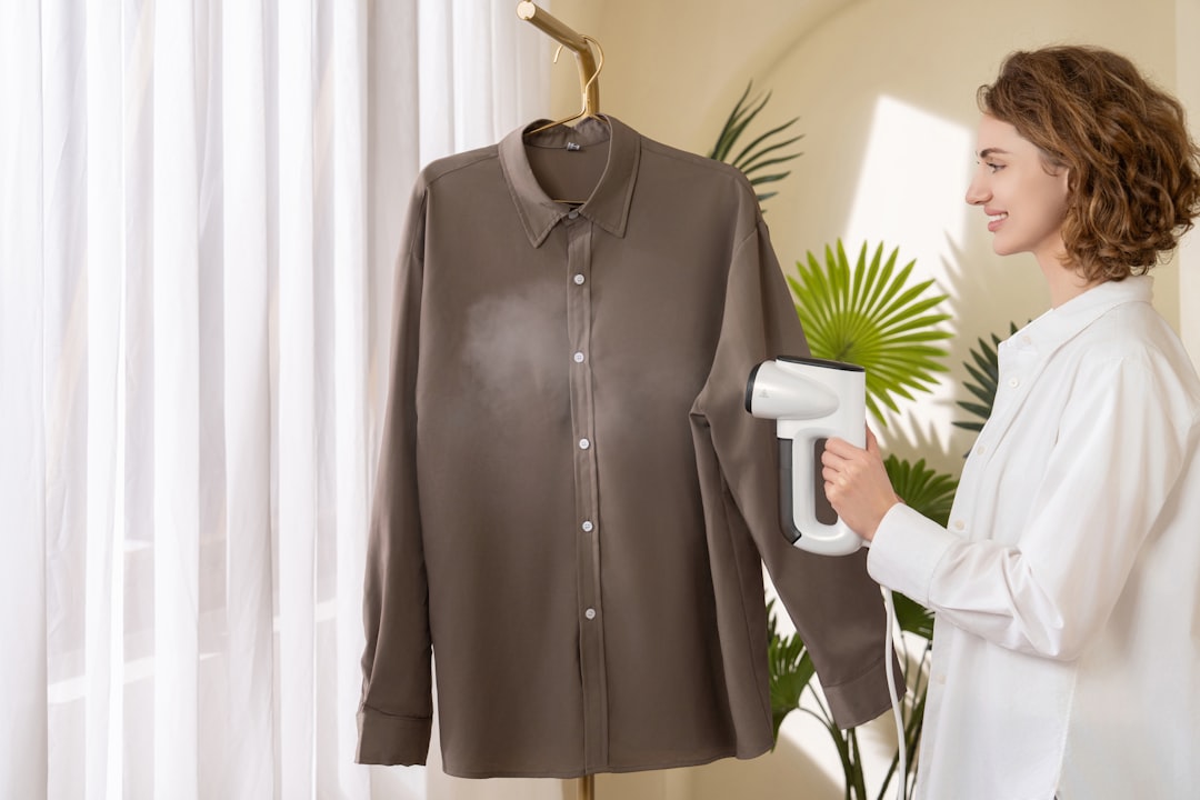 Woman smiling while using a handheld steamer to remove wrinkles from a hanging shirt without an iron