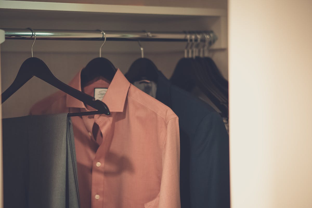 Dress shirts and pants hanging on hangers in a closet, demonstrating the hang-and-wait method for removing light wrinkles from clothes